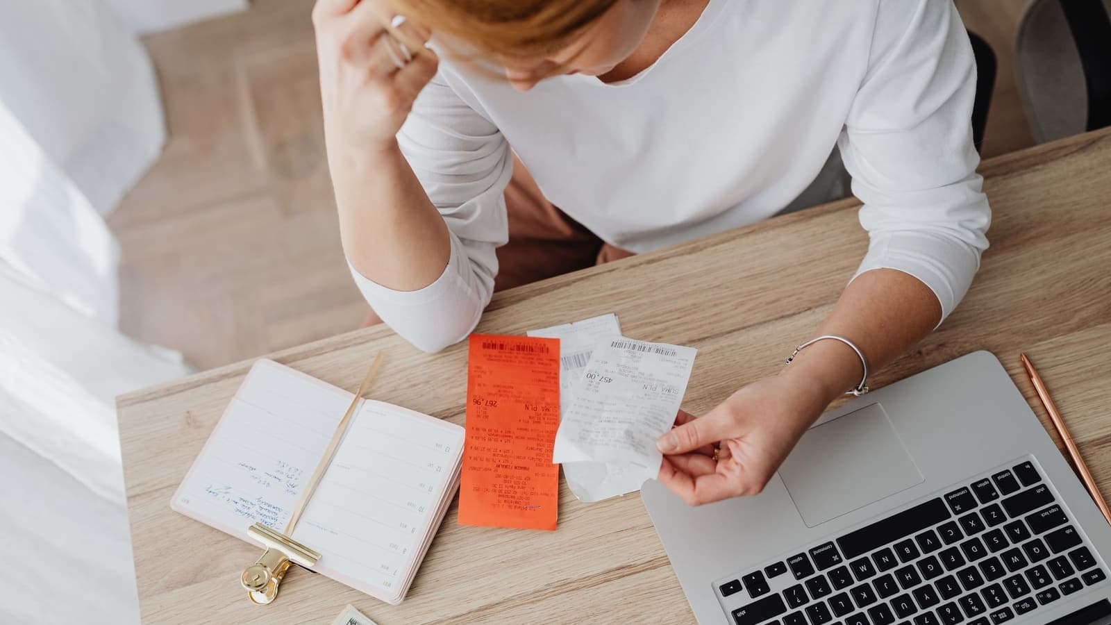 A small business owner going through receipts and a notebook next to a laptop while planning a website budget.