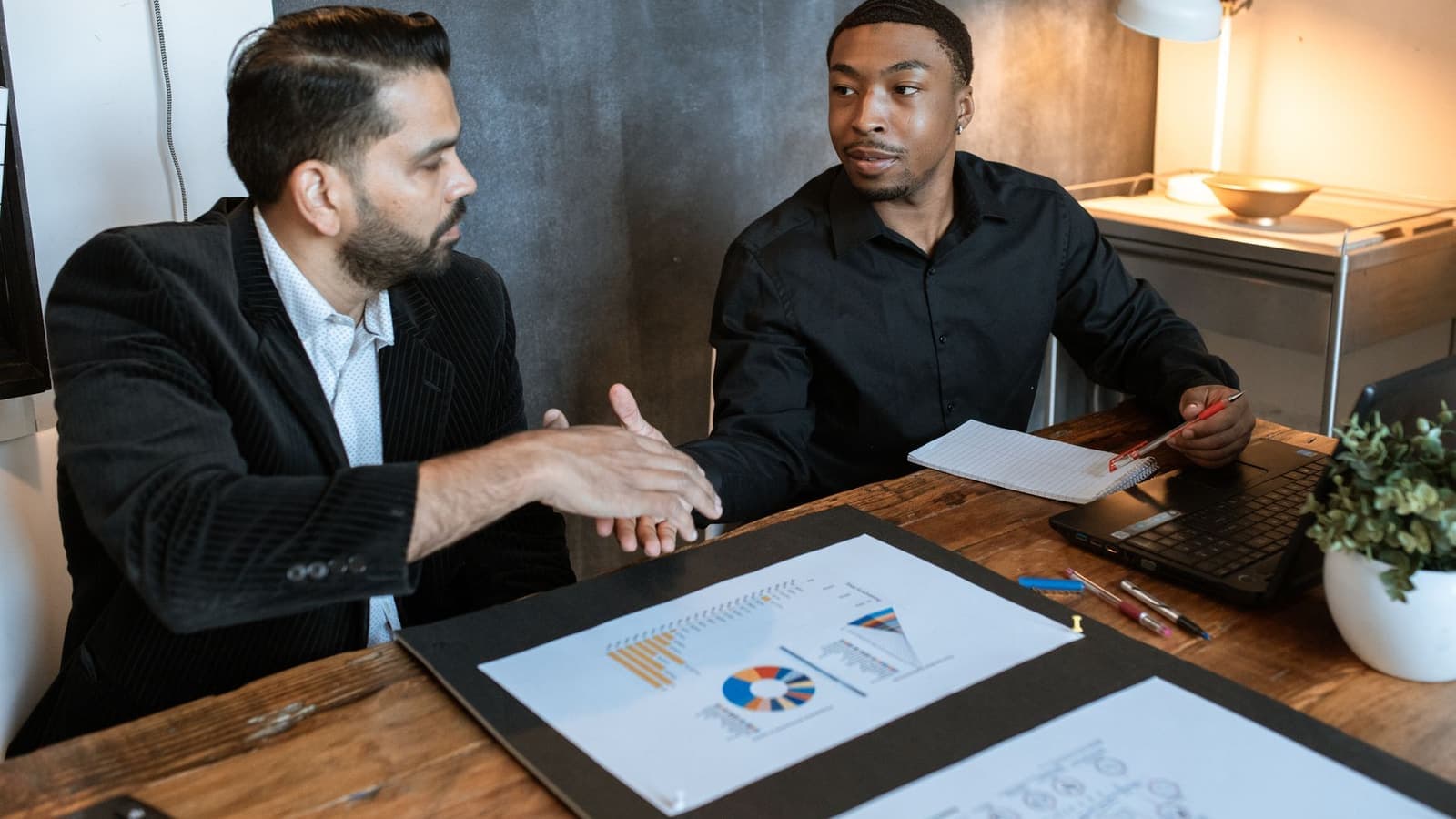 A business owner shaking hands with a consultant over a desk covered in marketing charts.