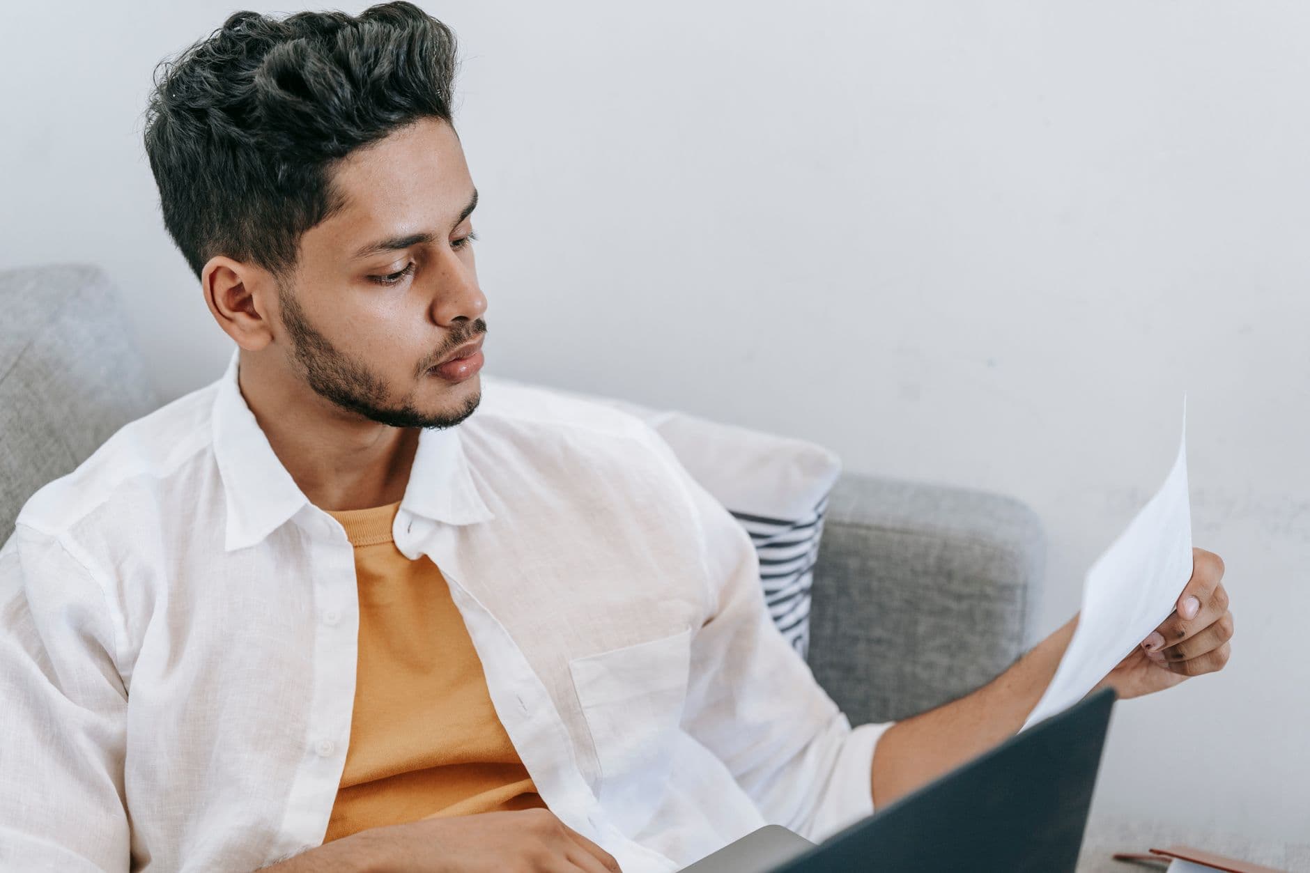 A small business owner on a couch reading a printed SEO audit report next to his laptop