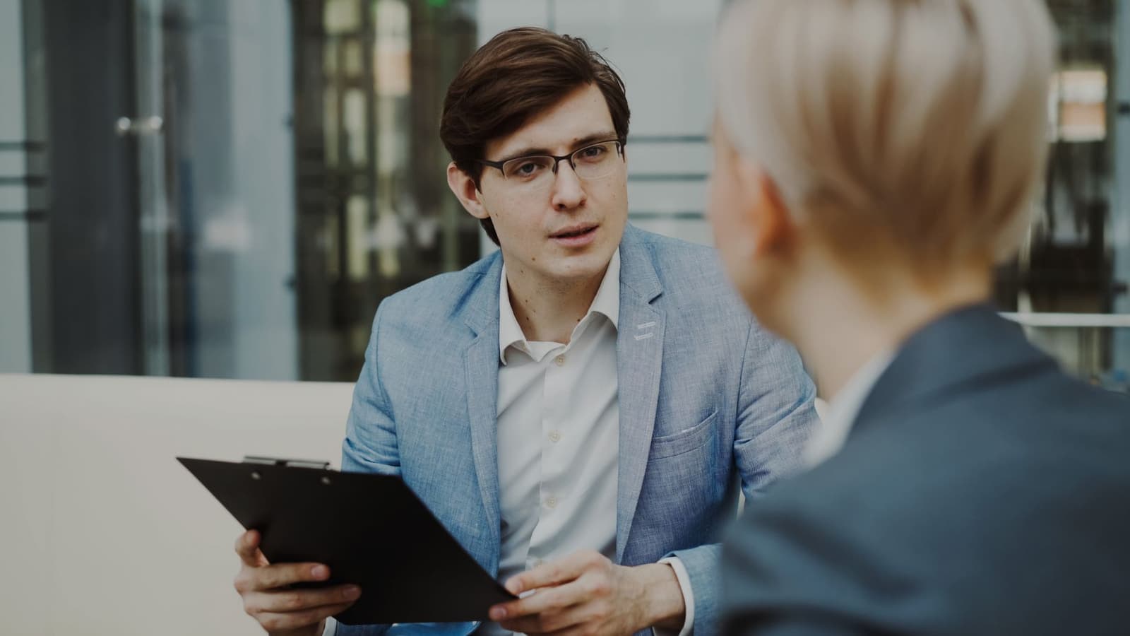 A web consultant with a clipboard listening to a client's questions during an office meeting.