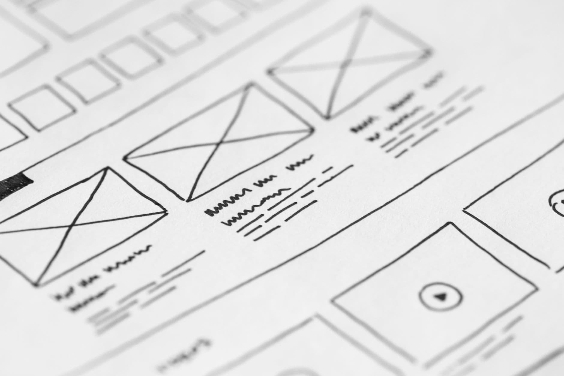 A hand-drawn website wireframe sketch on paper, showing boxes for a header, hero image, and content sections.