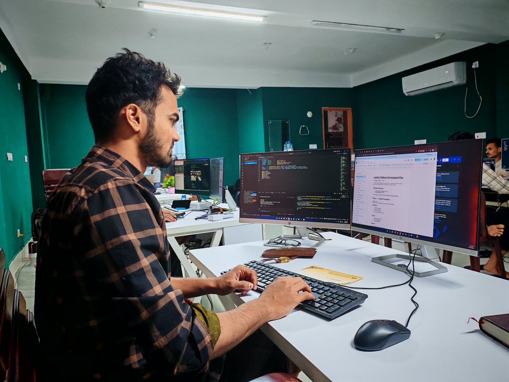 A software developer working at a dual-monitor desk, writing custom code for a client site instead of configuring a WordPress theme