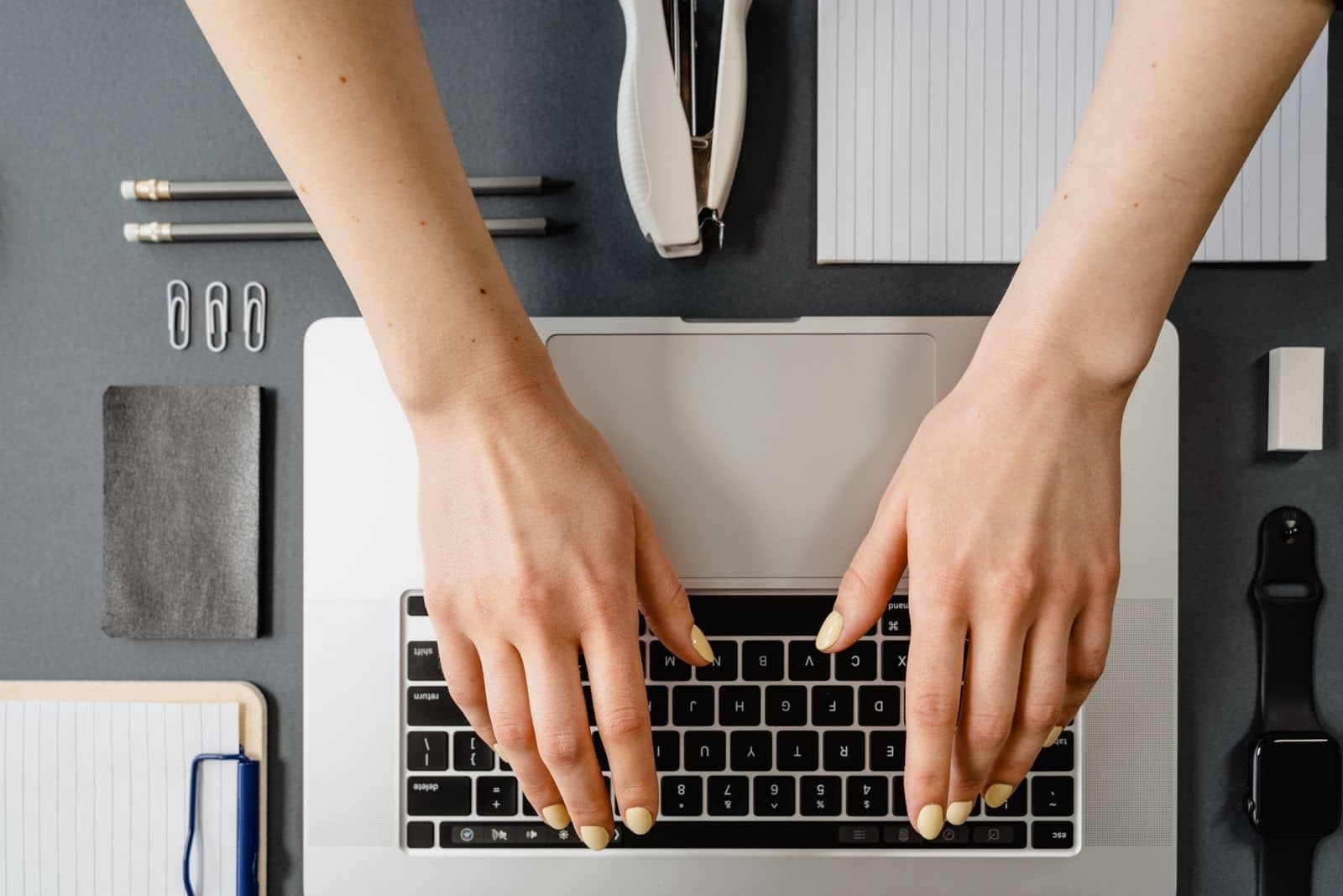 Writer's hands typing on a laptop keyboard surrounded by a notebook, pencils, and stationery, mid-draft on a blog post