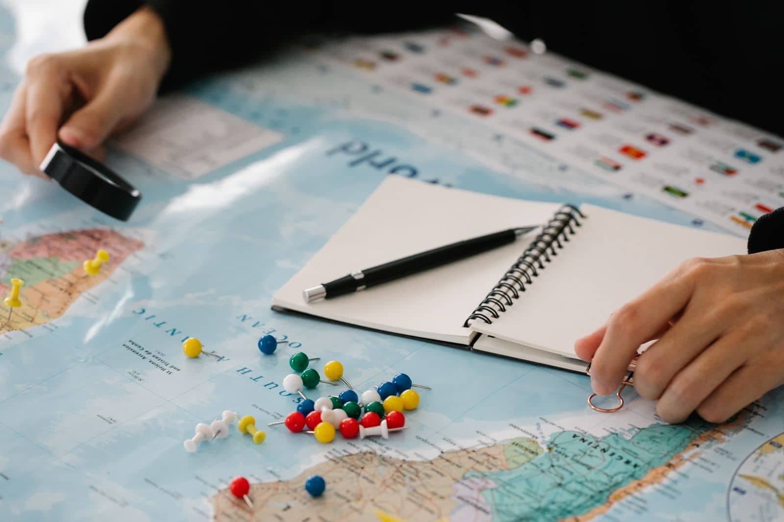 Una libreta, un bolígrafo y alfileres de colores sobre un mapa, como cuando se planea a dónde va cada página vieja en un sitio nuevo