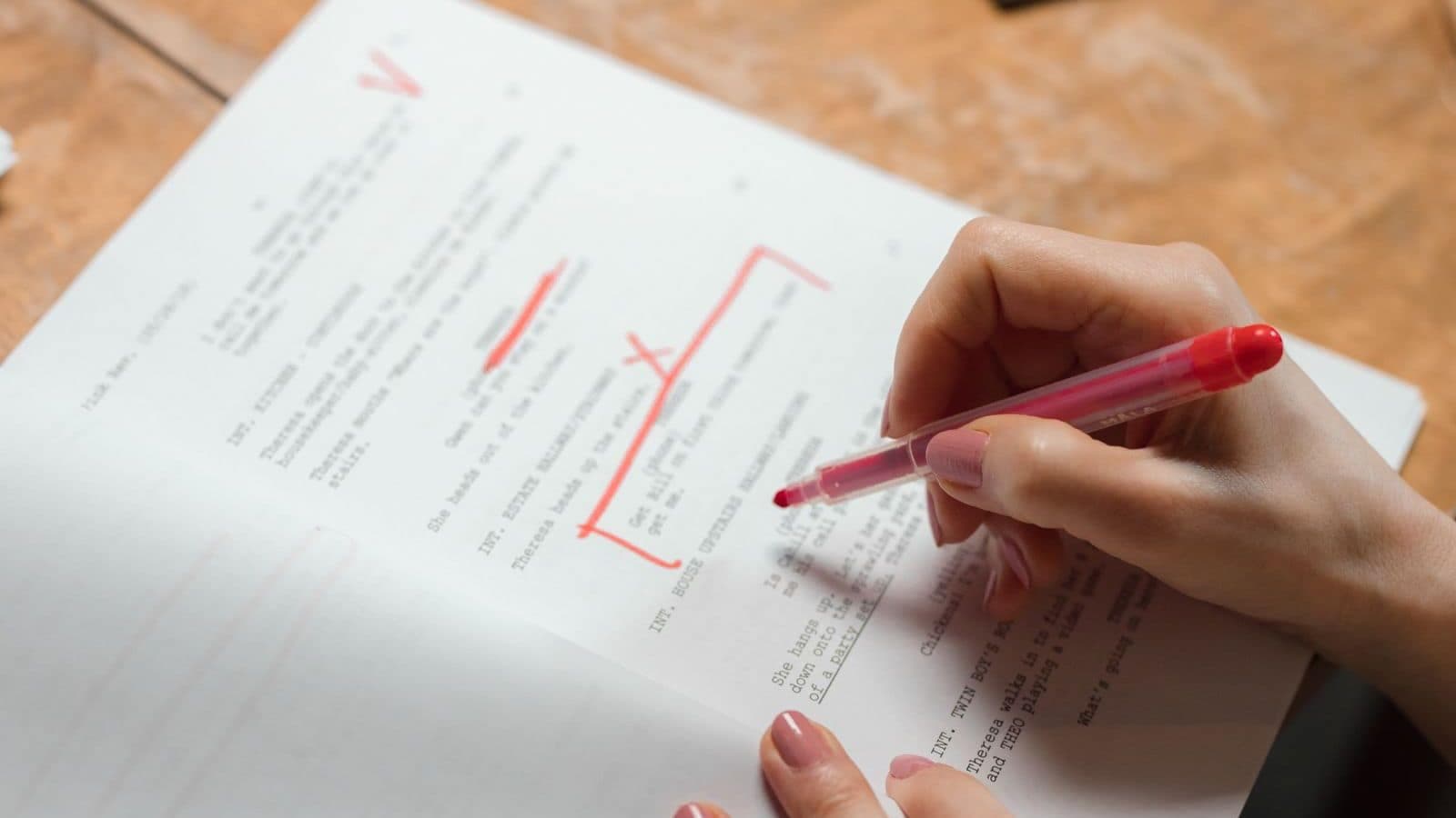 A close-up of a hand marking script copy with a red pen, editing and refining the wording line by line