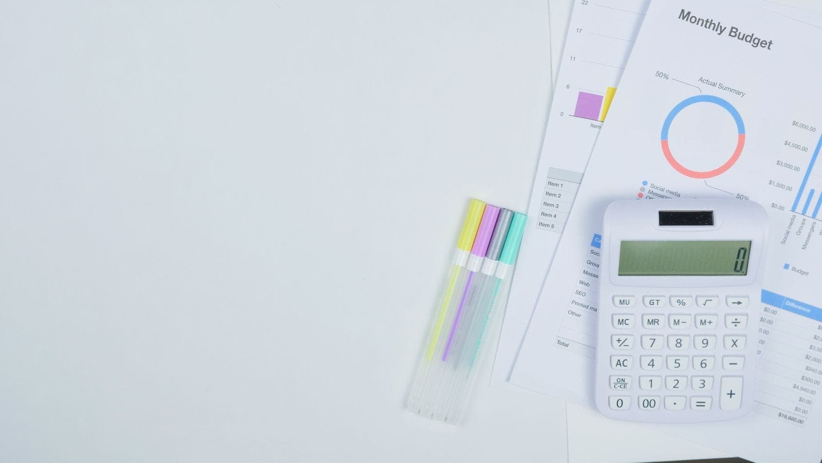 Calculator and monthly budget summary sheet laid out on a desk with colored pens