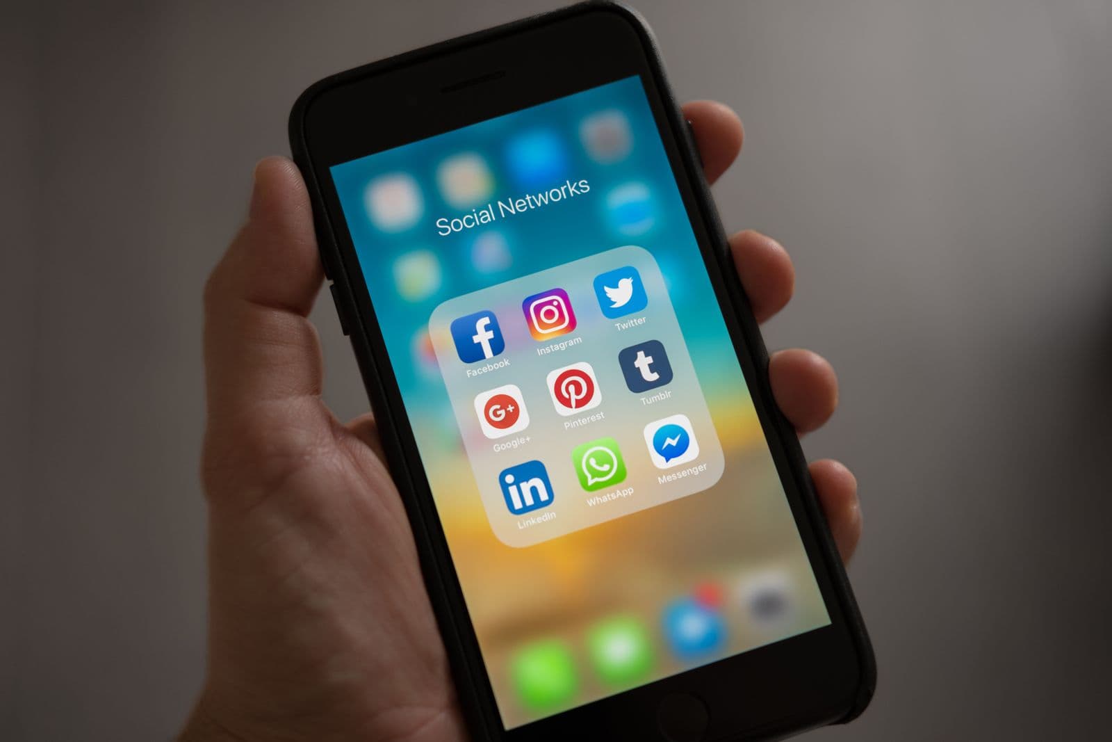 A hand holding a phone showing a folder of social media apps - Facebook, Instagram, LinkedIn, and more