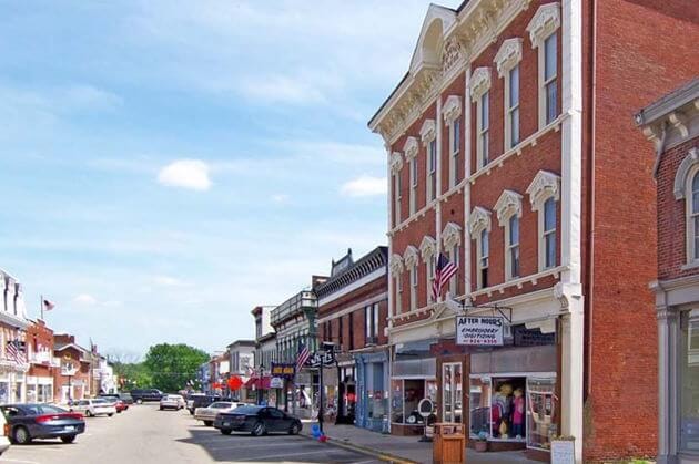 Historic Main Street in Bryant, Indiana featuring local small businesses, brick storefronts, and American flags hanging along the street on a sunny day