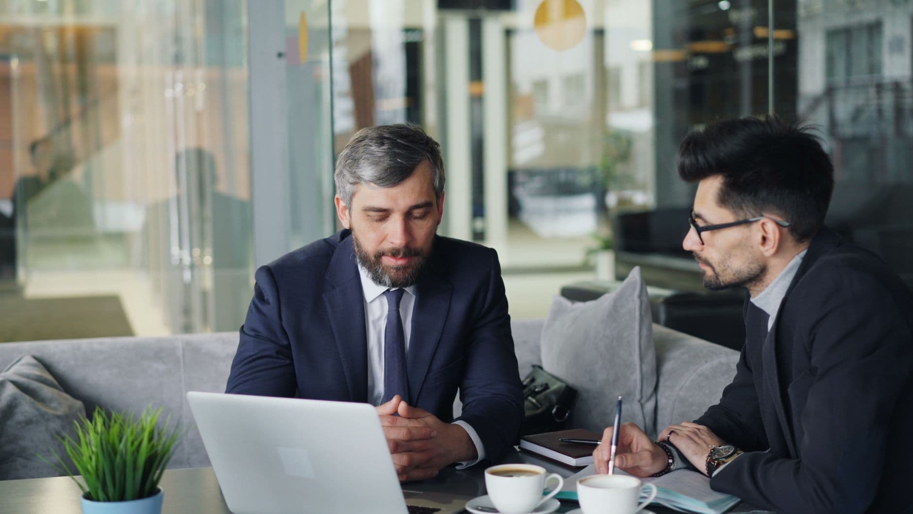 A small business owner in a discovery meeting with a web design consultant, reviewing plans on a laptop