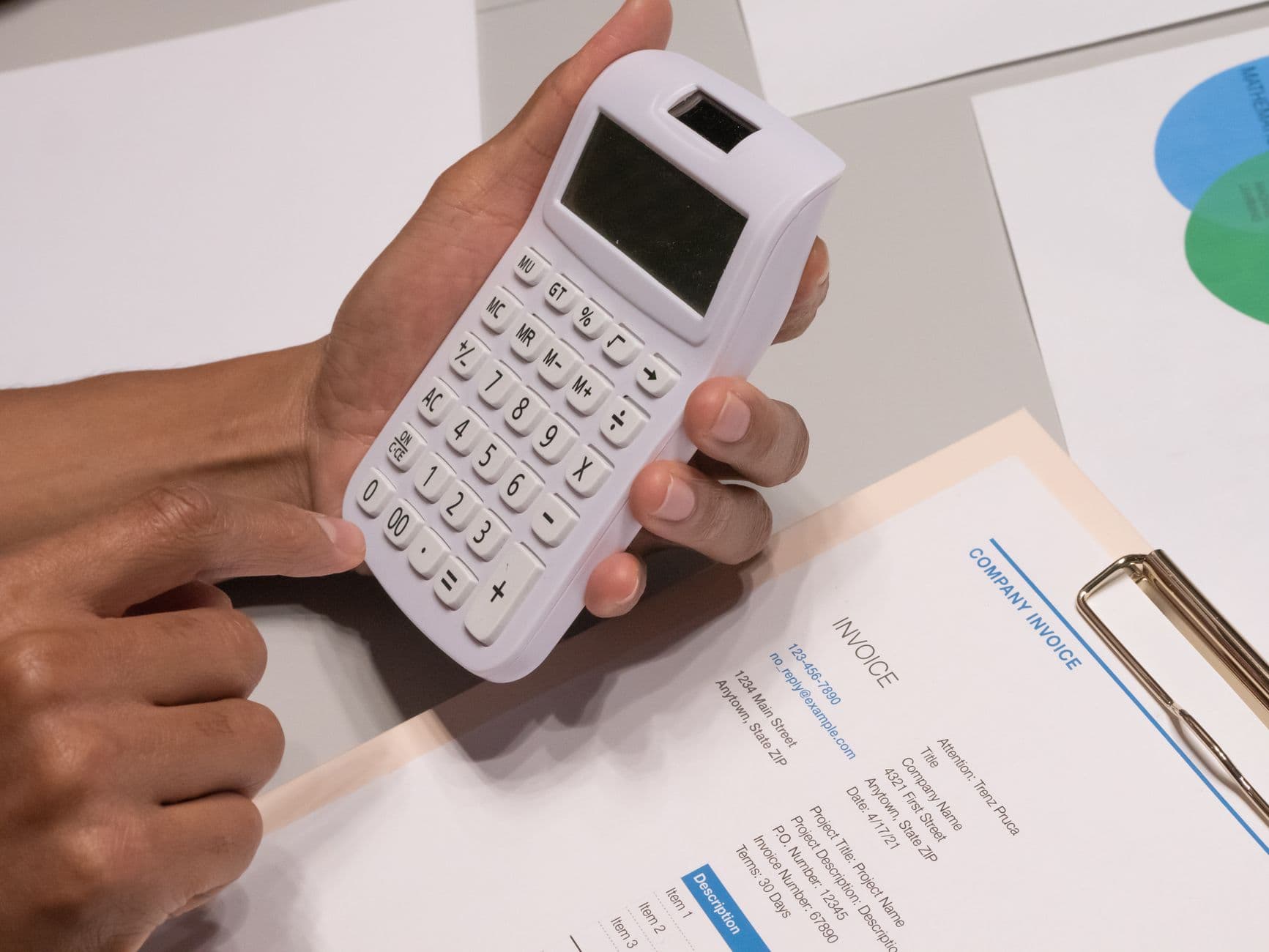 Close-up of hands using a calculator next to a company invoice, working out a real website budget